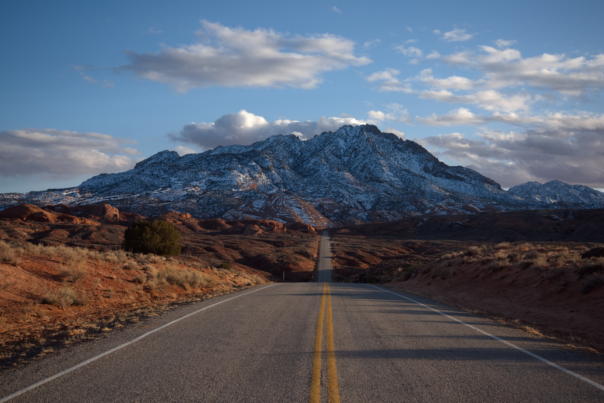 Lonely road in a desert landscape heading toward a low snow covered mountain. 